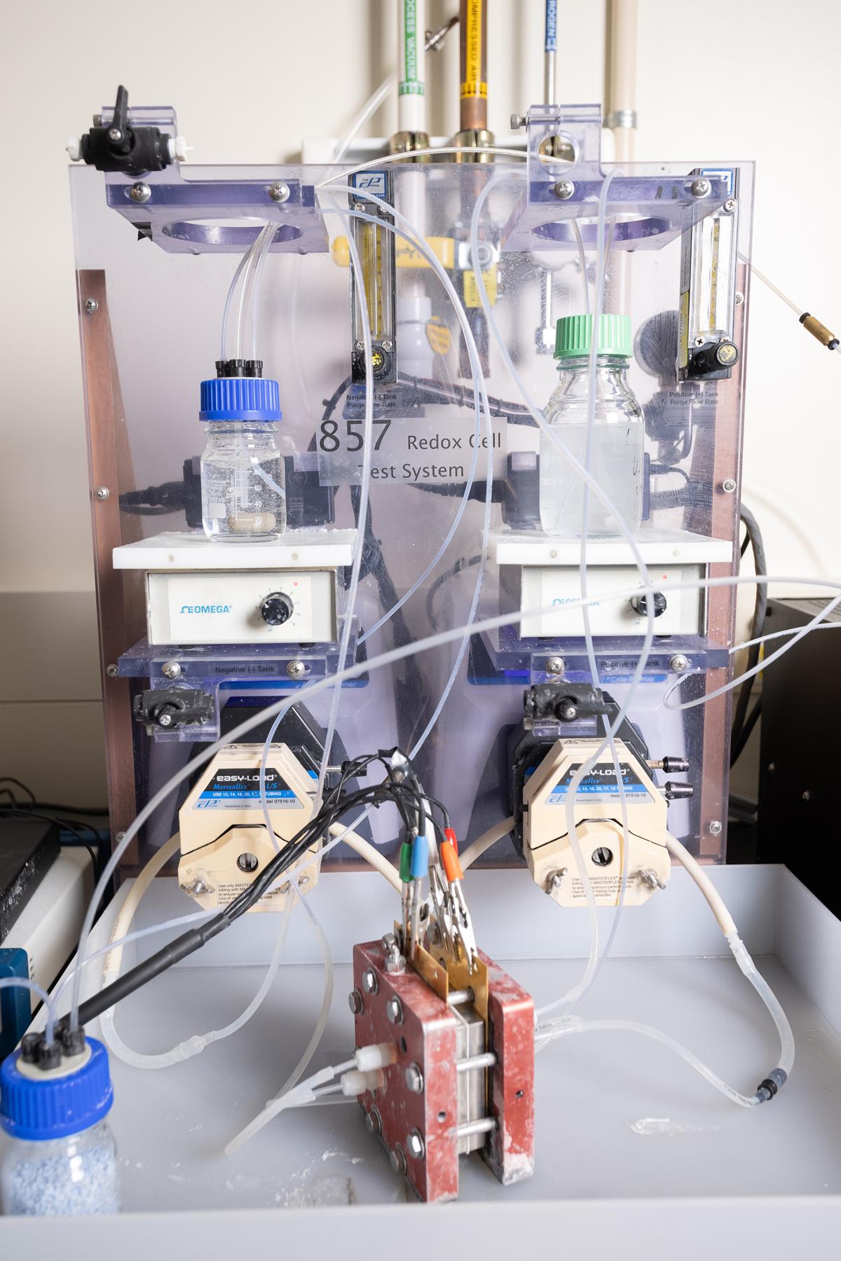 An experimental setup in the lab with a tubes, vials, and a small, reddish-orange square, electrochemical reactor prototype.